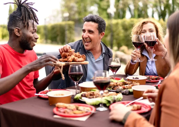 Imagem de um grupo de pessoas sentados ao redor de uma mesa enquanto comem, brindam taças de vinho e se divertem para ilustrar matéria sobre as melhores churrascarias de São Paulo