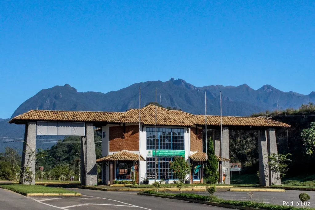 Imagem de um prédio com telhado de telhas e grandes colunas fica em uma entrada, cercado por vegetação e altas montanhas, em Peno, no interior do Rio de Janeiro