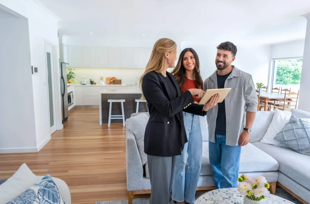 Imagem de um casal formado por um homem e uma mulher visitando um imóvel na companhia de uma corretora imobiliária para ilustrar matéria sobre qual a melhor forma de captar imóveis