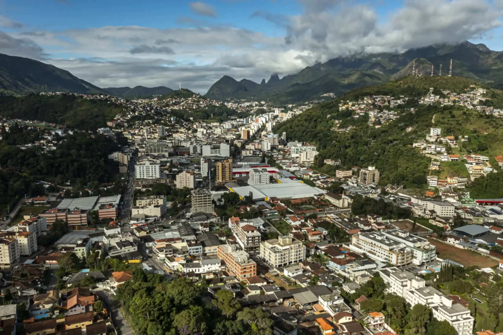 Imagem da vista aérea de Teresópolis, no Rio de Janeiro, mostra colinas e montanhas verdes com vários edifícios, estradas e vegetação