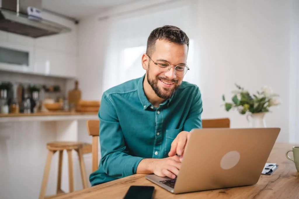 Imagem de um homem de barba e óculos sentado em frente a um notebook na cozinha de casa para ilustrar matéria sobre a isenção de IPTU para idosos em Salvador