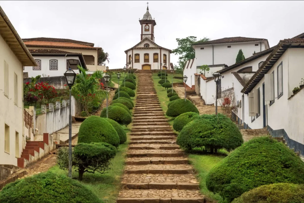 Imagem de uma escada, casas e igreja em estilo colonial na cidade de Serro para ilustrar matéria sobre as cidades históricas de MG