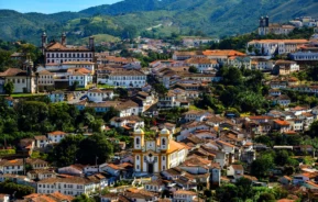 Imagem da vista de uma cidade histórica colonial onde construções dividem espaço com a vegetação da montanha para ilustrar matéria sobre as cidades históricas de Minas Gerais