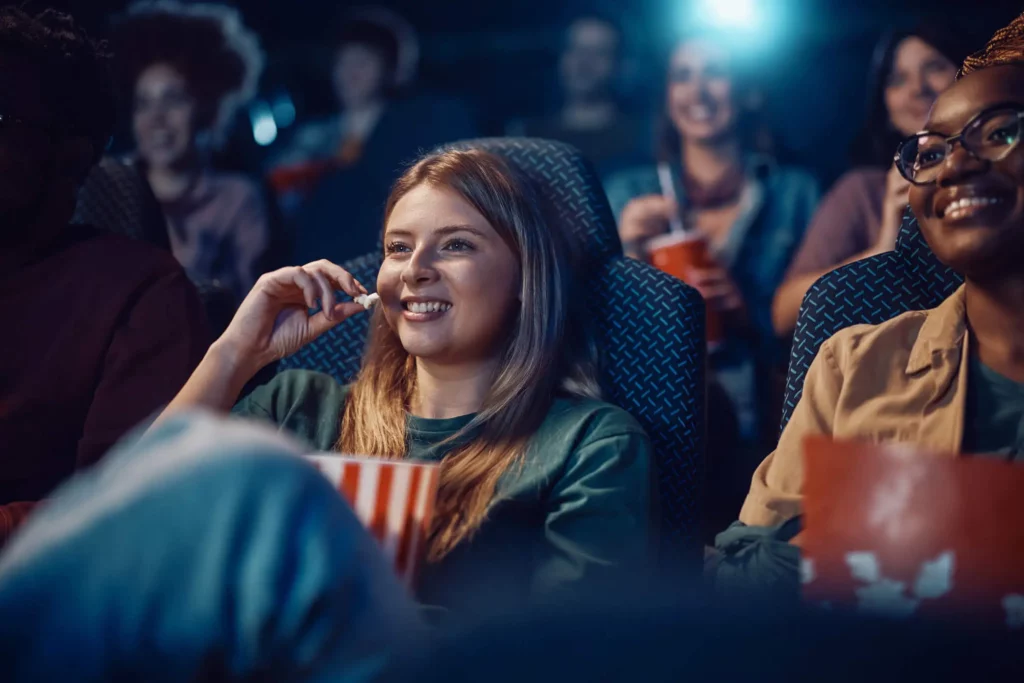 Imagem de uma jovem feliz comendo pipoca em uma sala de cinema ao lado de uma amiga para ilustrar matéria sobre o que fazer no Shopping Eldorado