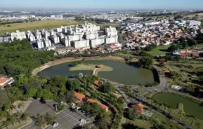 Imagem da vista aérea de um parque em Campinas mostra lago, vegetação e prédios ao fundo para ilustrar matéria sobre os parques ecológicos em Campinas