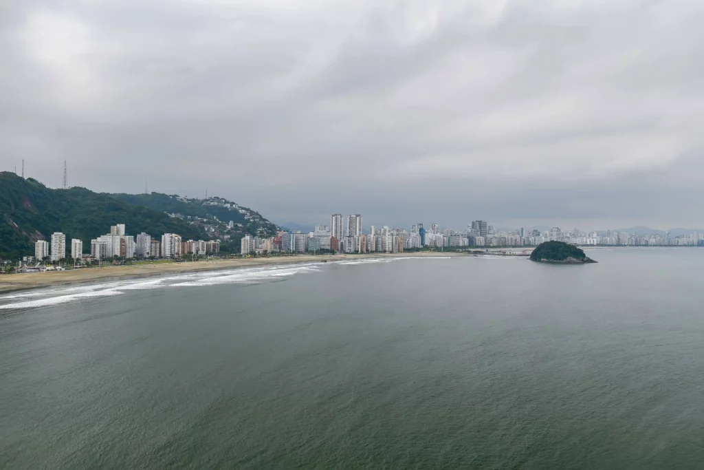 Imagem da paisagem de São Vicente mostra mar, faixa de areia e prédios ao fundo para ilustrar matéria sobre bairro em São Vicente