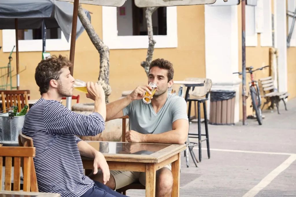 Imagem de dois amigos sentados em uma mesa de bar tomando cerveja para ilustrar matéria sobre os melhores bares de BH