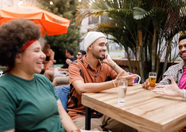 Imagem de um grupo de amigos sentados ao redor de uma mesa de madeira conversando sobre bebidas para ilustrar matéria sobre os melhores bares de BH para conhecer