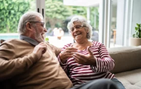 Foto que ilustra matéria sobre Senior Living mostra um casal de um homem e uma mulher idosos sentados em um sofá e conversando sorridentes (Foto: Getty Images)