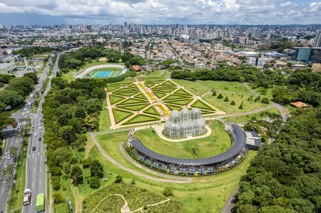 Imagem aérea da estufa no Jardim Botânico de Curitiba mostra vista do parque e prédios da cidade ao fundo