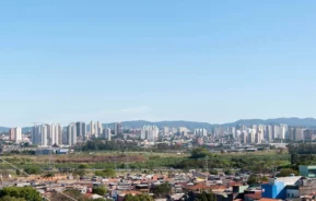 Imagem da vista aérea de Guarulhos mostra casas, vegetação e prédios ao fundo em um dia de céu azul para ilustrar matéria sobre o custo de vida em Guarulhos