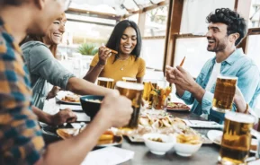 Imagem de amigos sentados ao redor de uma mesa com comidas e bebidas para ilustrar matéria sobre os melhores bares da Vila Olímpia