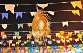 Imagem de um chapéu de palha pendurado em bandeirinhas de festa junina para ilustrar matéria sobre quermesse em SP