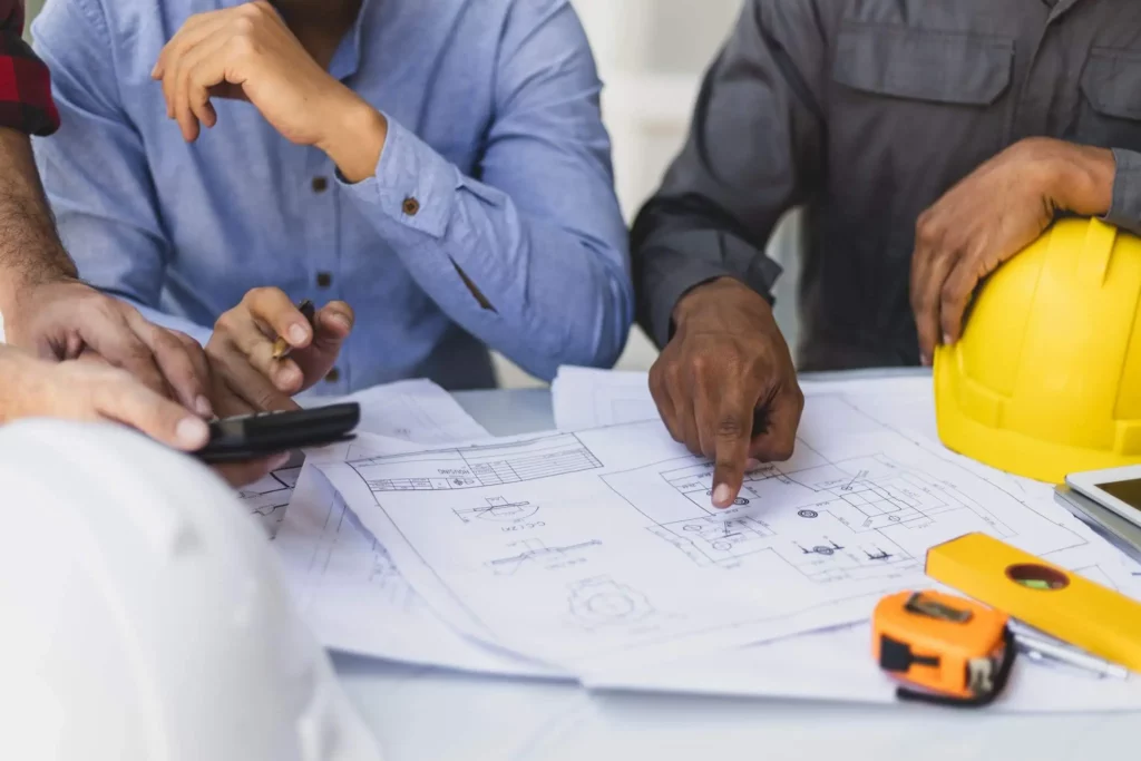 Imagem de pessoas ao redor de uma mesa com papéis relacionados a um imóvel e equipamentos de construção para ilustrar matéria sobre como averbar a construção de um imóvel na matrícula