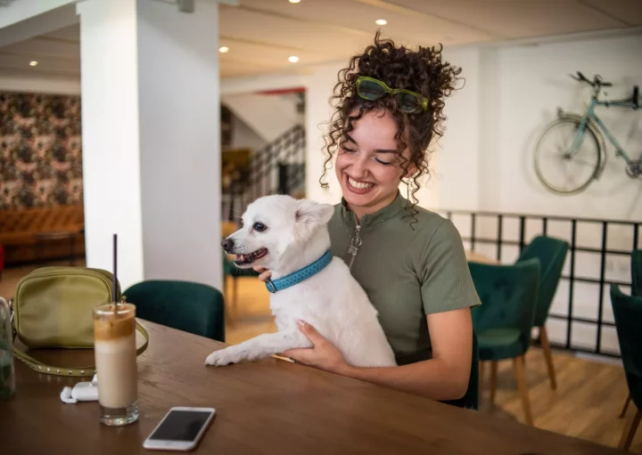 Uma mulher sorridente em um restaurante pet friendly sentada à mesa e com seu cachorro no colo