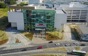 Vista aérea do Shopping Cidade Sorocaba, um dos principais shoppings em Sorocaba, com janelas de vidro, um estacionamento, palmeiras e carros circulando nas ruas próximas.
