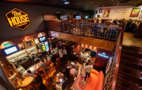 Foto mostrando a parte interna do The House Food & Fun com ângulo amplo podendo visualizar o salão no primeiro e segunda andar. O local é um bar temático em BH, parte dos dez mais famosos do segmento