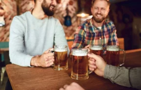 Imagem de um grupo de amigos sentados na mesa de um bar conversando e segurando uma caneca de chopp para ilustrar matéria sobre os melhores bares em Curitiba