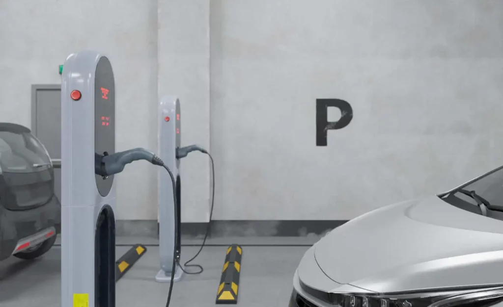 Imagem de dois veículos elétricos estacionados e carregando em estações de recarga internas em um estacionamento. 