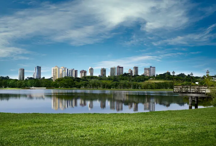 Imagem de parque e lago em Curitiba com vista para prédios ao fundo em um dia de céu azul