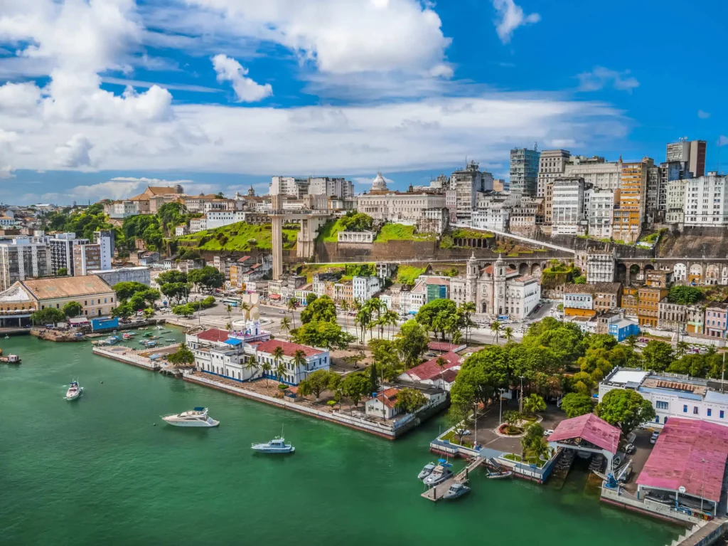 Imagem da vista aérea de Salvador mostra barcos, mar, prédios e vegetação em um dia de céu azul