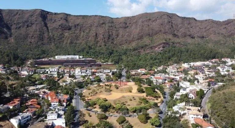 Vista aérea de um bairro residencial com casas e vegetação na base de uma grande cadeia de montanhas rochosas da Serra do Curral