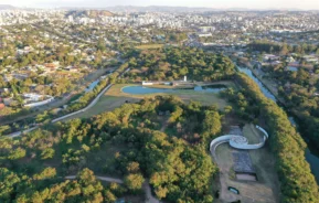 Imagem da vista aérea do Parque Ecológico da Pampulha mostrando exuberantes jardins verdes, caminhos sinuosos, edifícios modernos, fontes de água e uma paisagem urbana ao fundo sob um céu claro para ilustrar matéria sobre parque ecológico perto de Belo Horizonte.