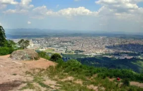 Imagem da vista do topo do Pico do Urubu, em Mogi das Cruzes, mostra a serra e os prédios da cidade em um dia de céu azul