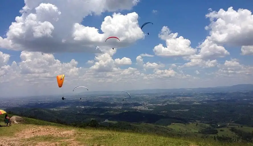 Imagem de vários parapentes sobrevoando a paisagem montanhosa do Pico do Urubu, em Mogi das Cruzes